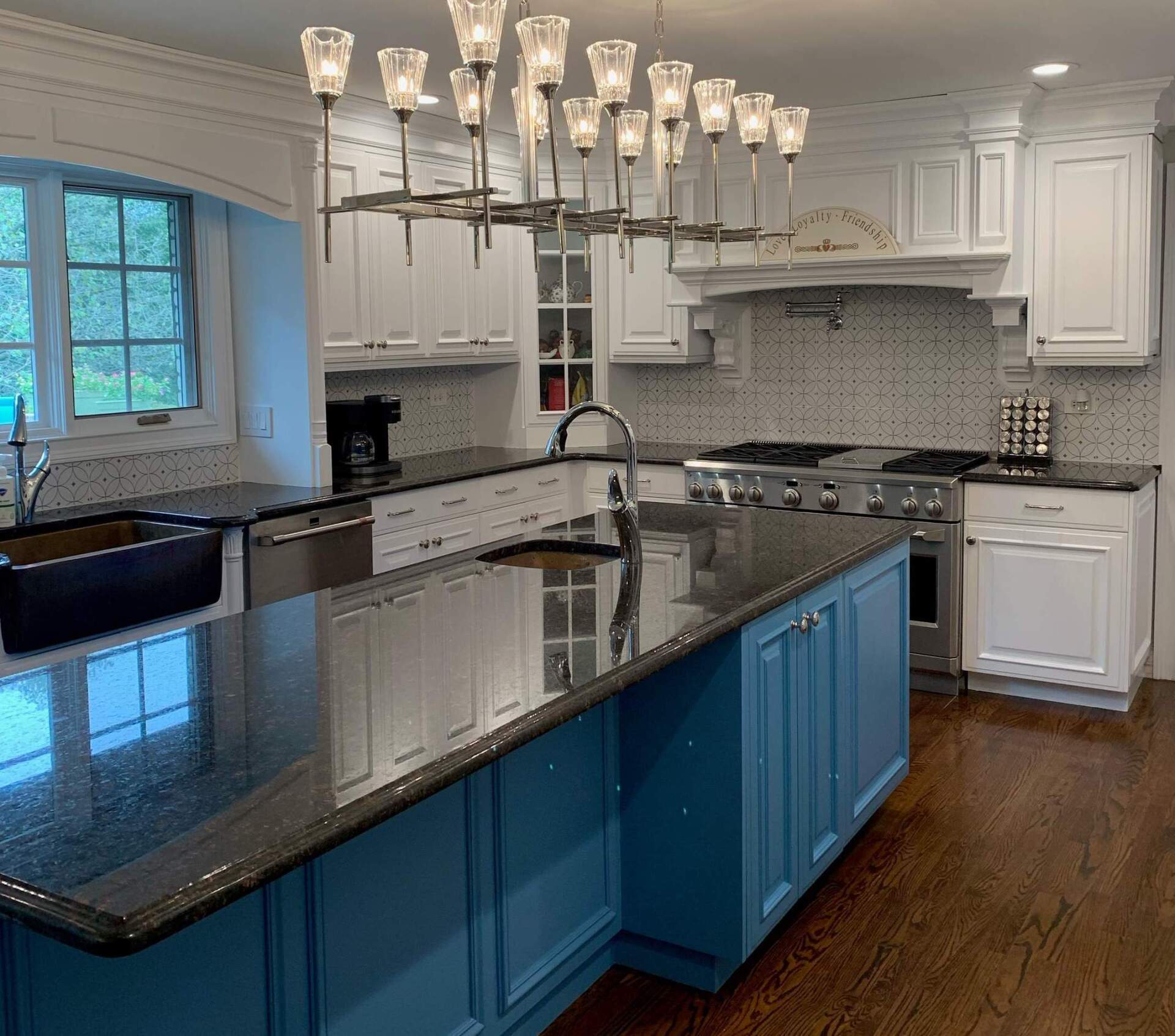 Bright kitchen with blue island, black countertops, white cabinets, and a chandelier.