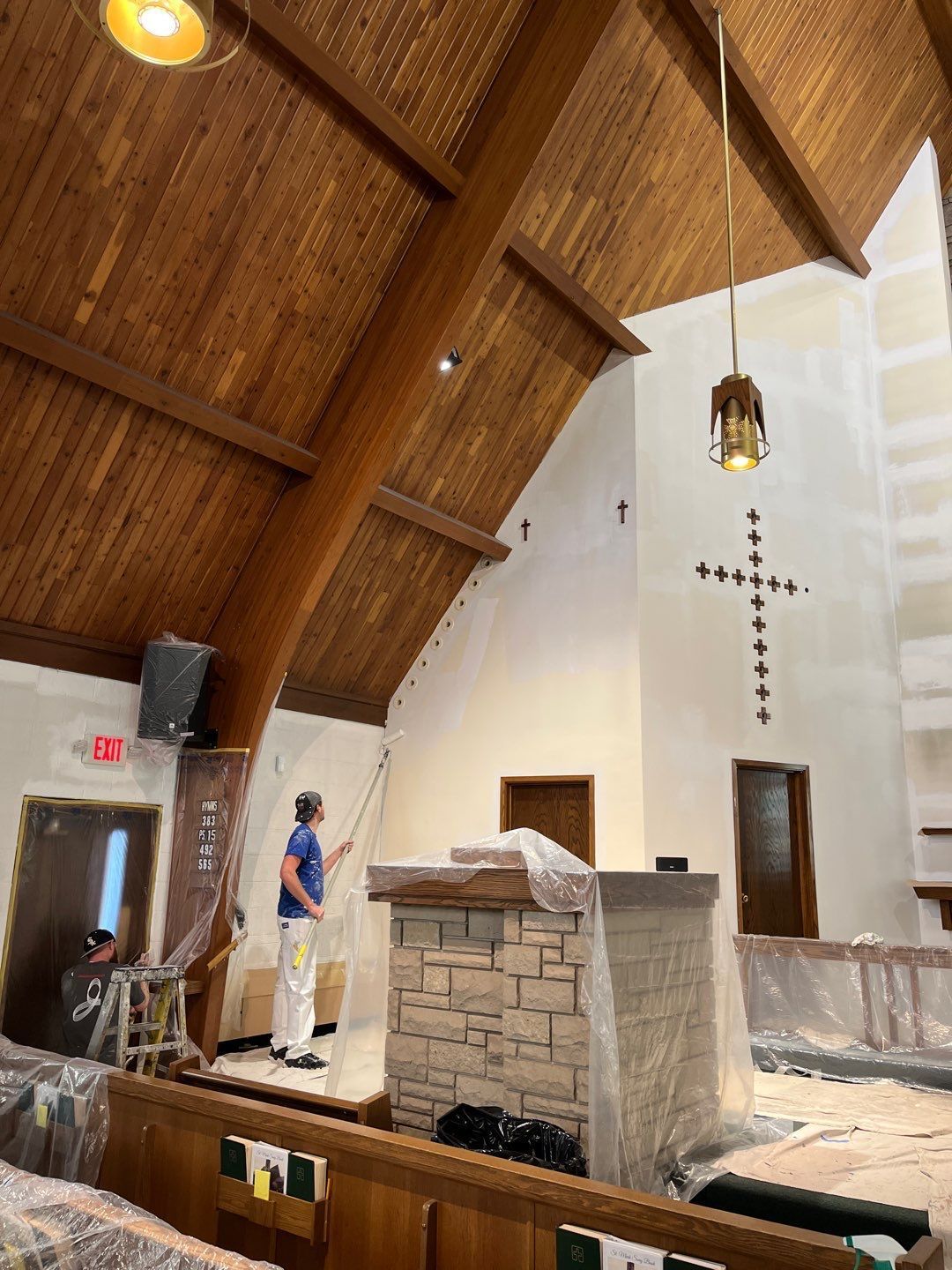 Church interior with vaulted wooden ceiling, altar area, and a person standing near the front.