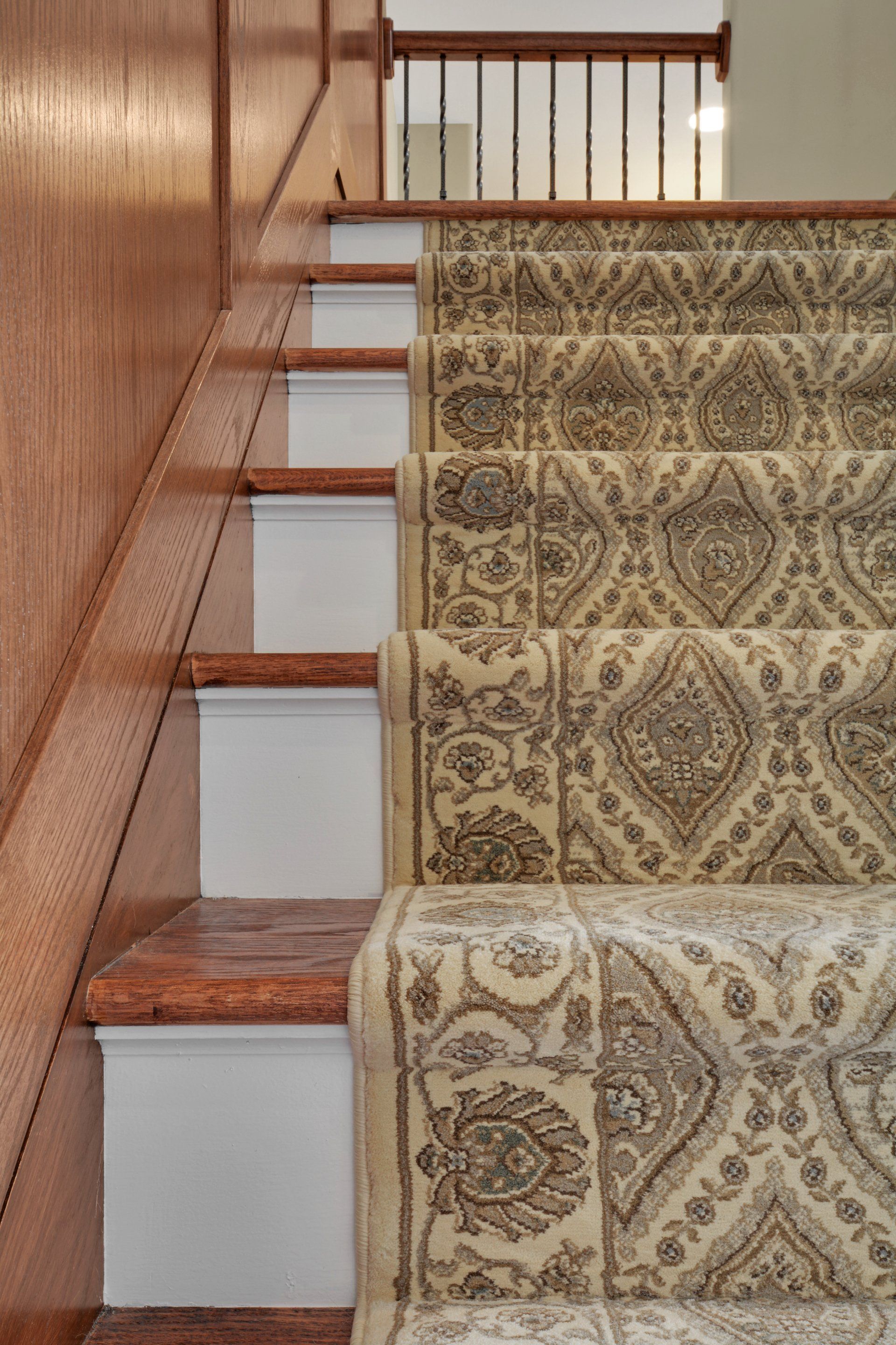 Carpeted wooden staircase with white risers and a brass railing beside a paneled wall