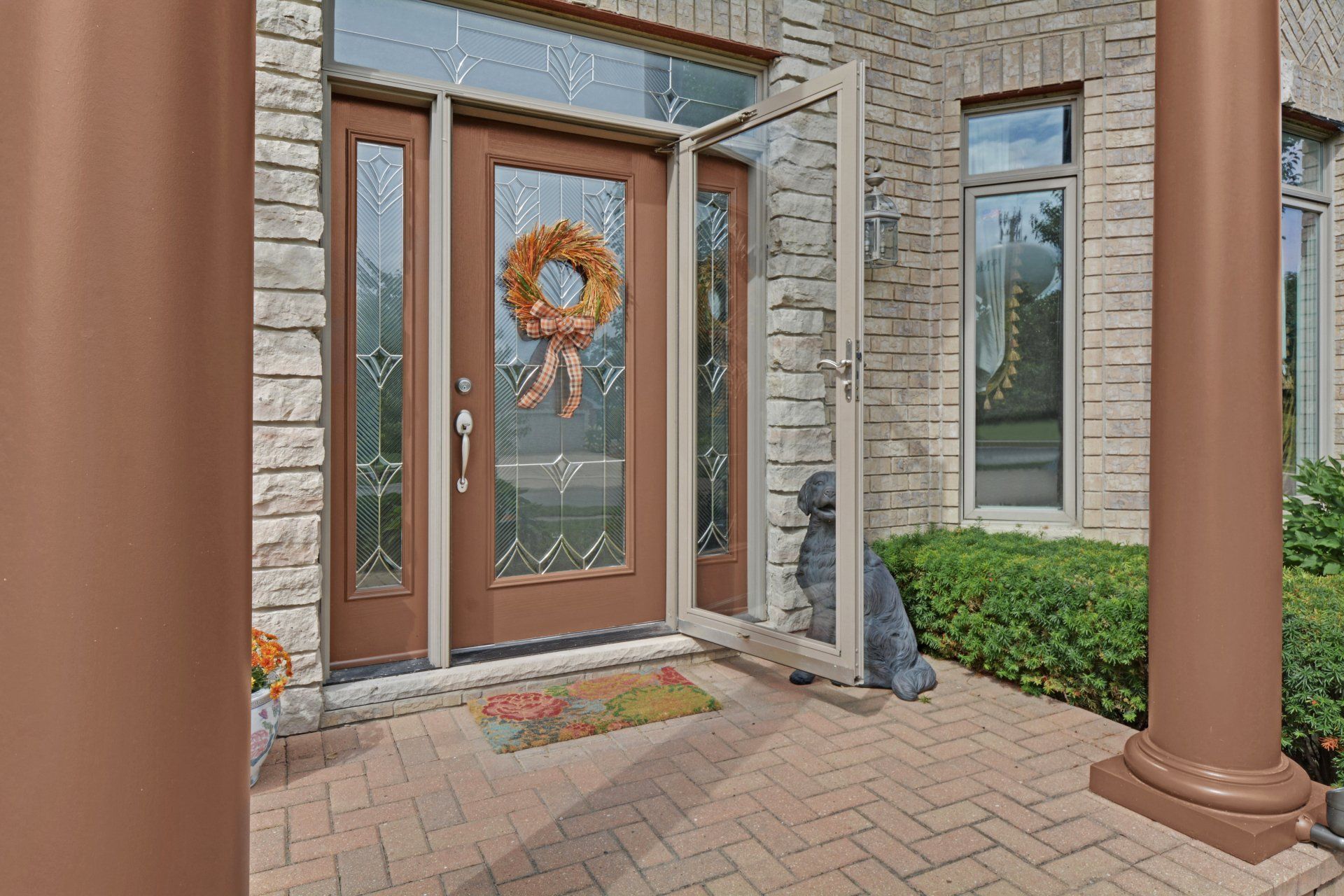 Front porch with glass double doors, autumn wreath, brick walkway, and stone columns.