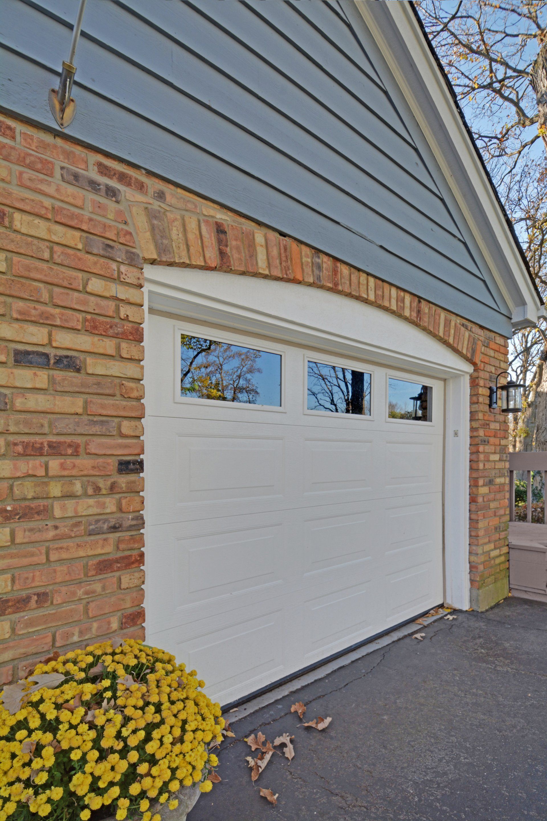 White garage door on a brick house with a yellow flower pot in front