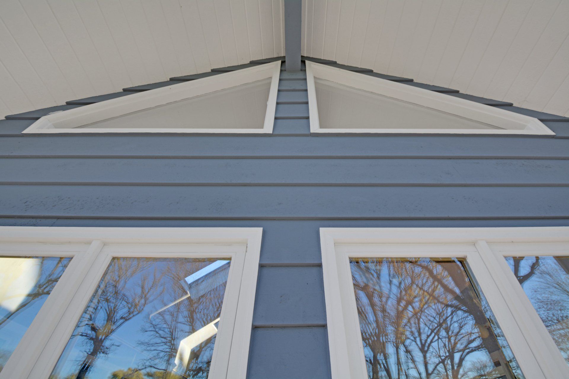 Blue house exterior with white-trimmed windows and steep roofline against a clear sky