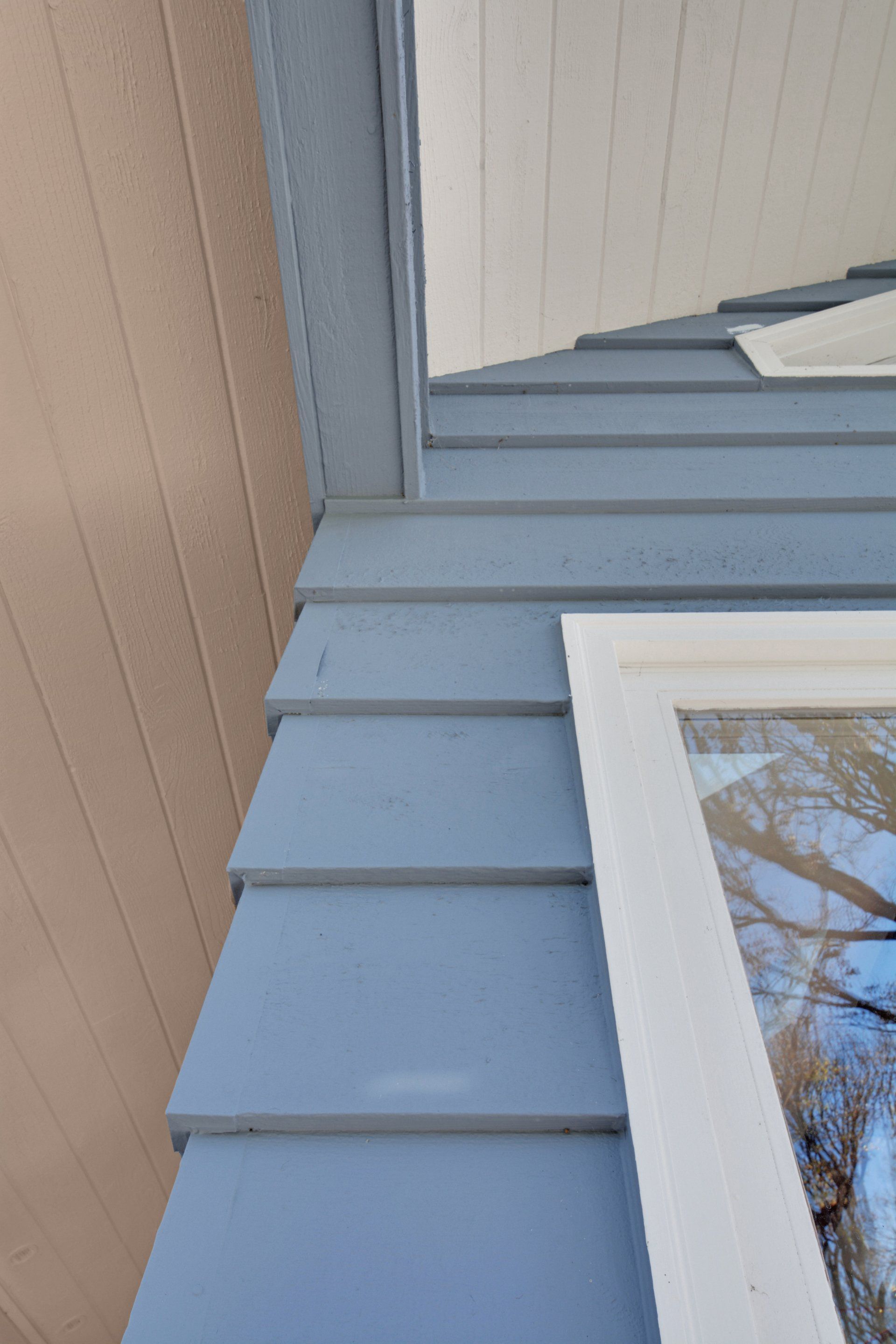 Blue house siding and white trim around a window, viewed close up at an angle.