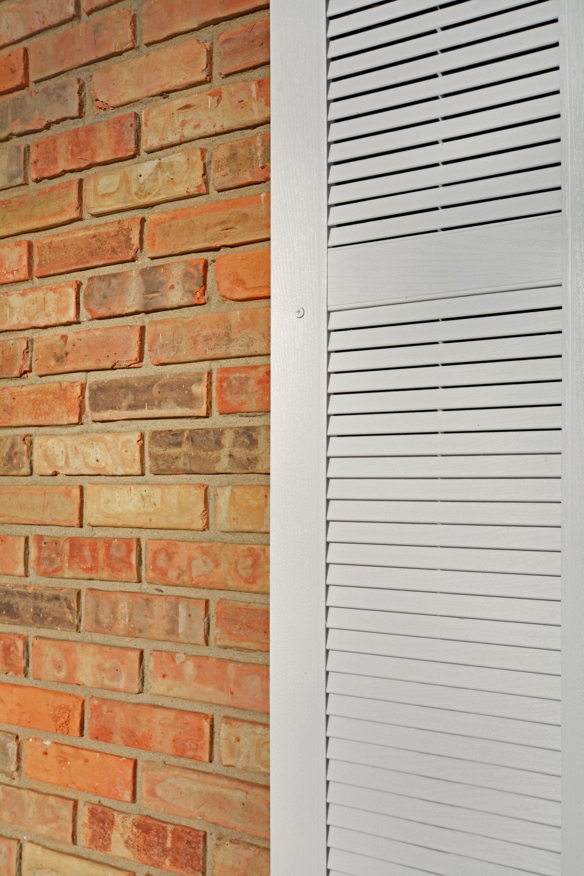 Red brick wall beside a white vented metal panel