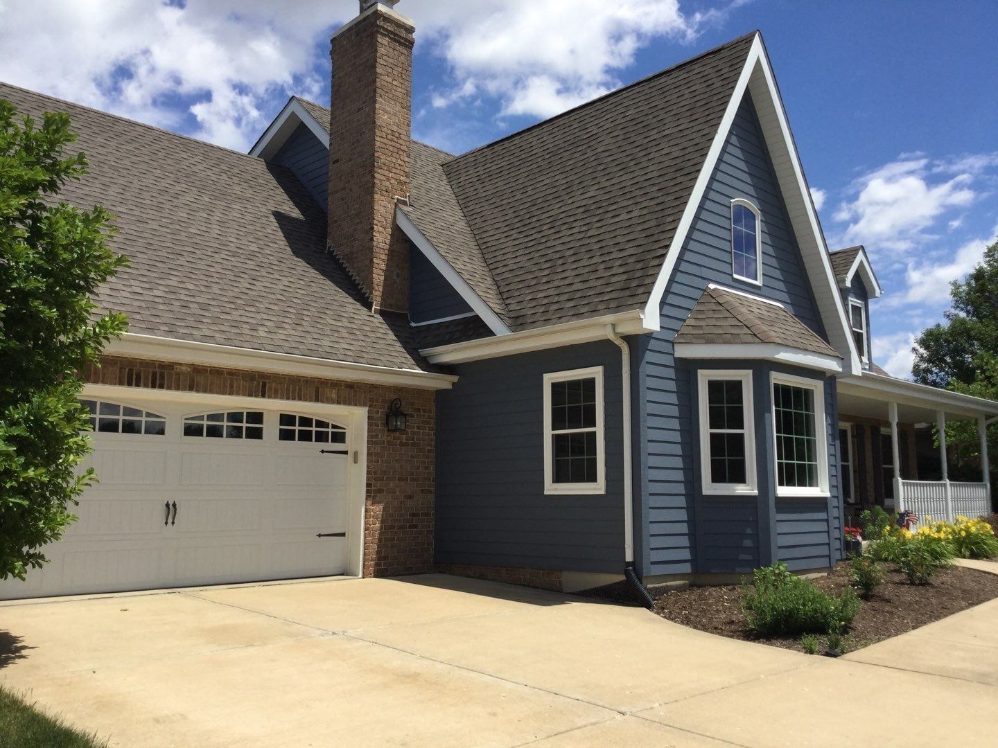 Blue house with white trim, brick chimney, and attached garage under a partly cloudy sky