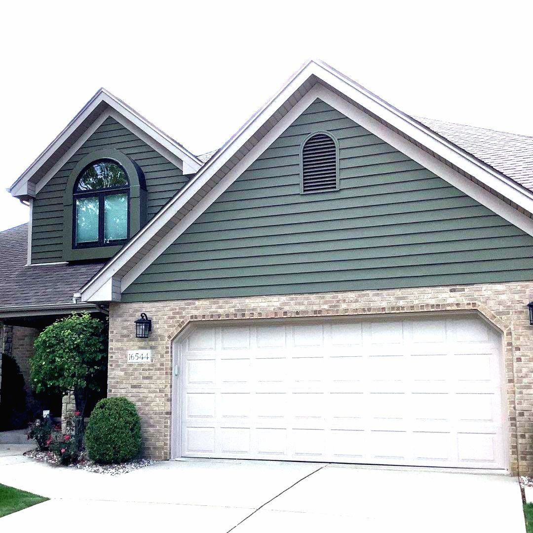 Suburban house exterior with a white garage door and green siding, front entrance and driveway visible