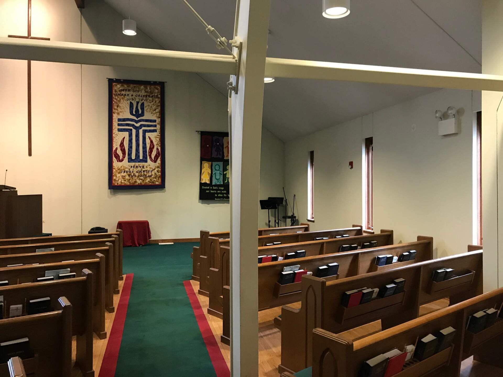 Church sanctuary with wooden pews, green aisle carpet, and wall banners near the altar