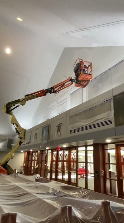 Construction lift reaching a high wall inside a building with protective plastic draped below.