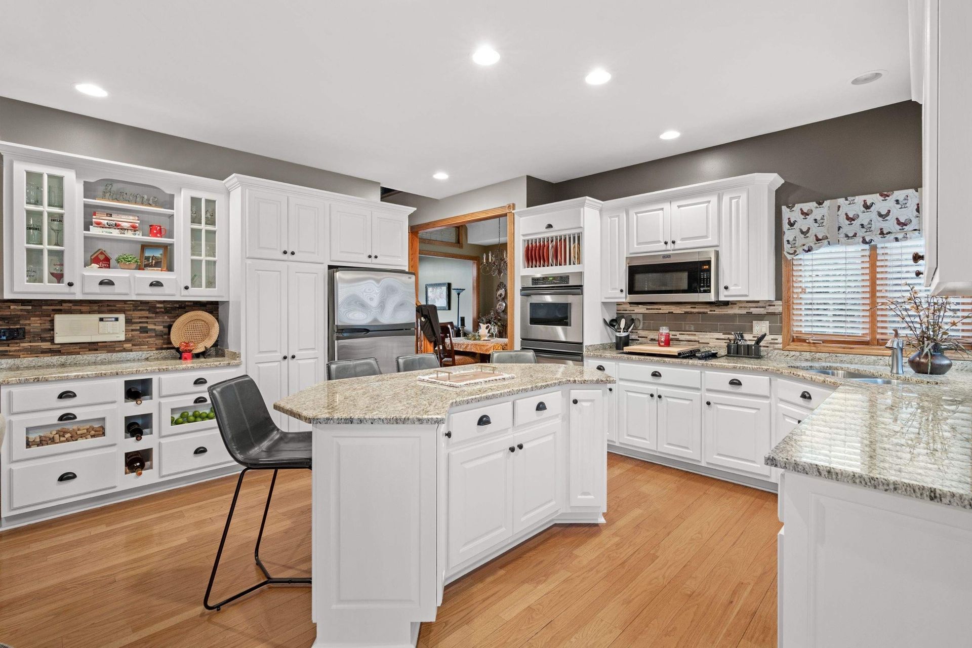 Bright white kitchen with granite counters, wood floors, and stainless steel appliances
