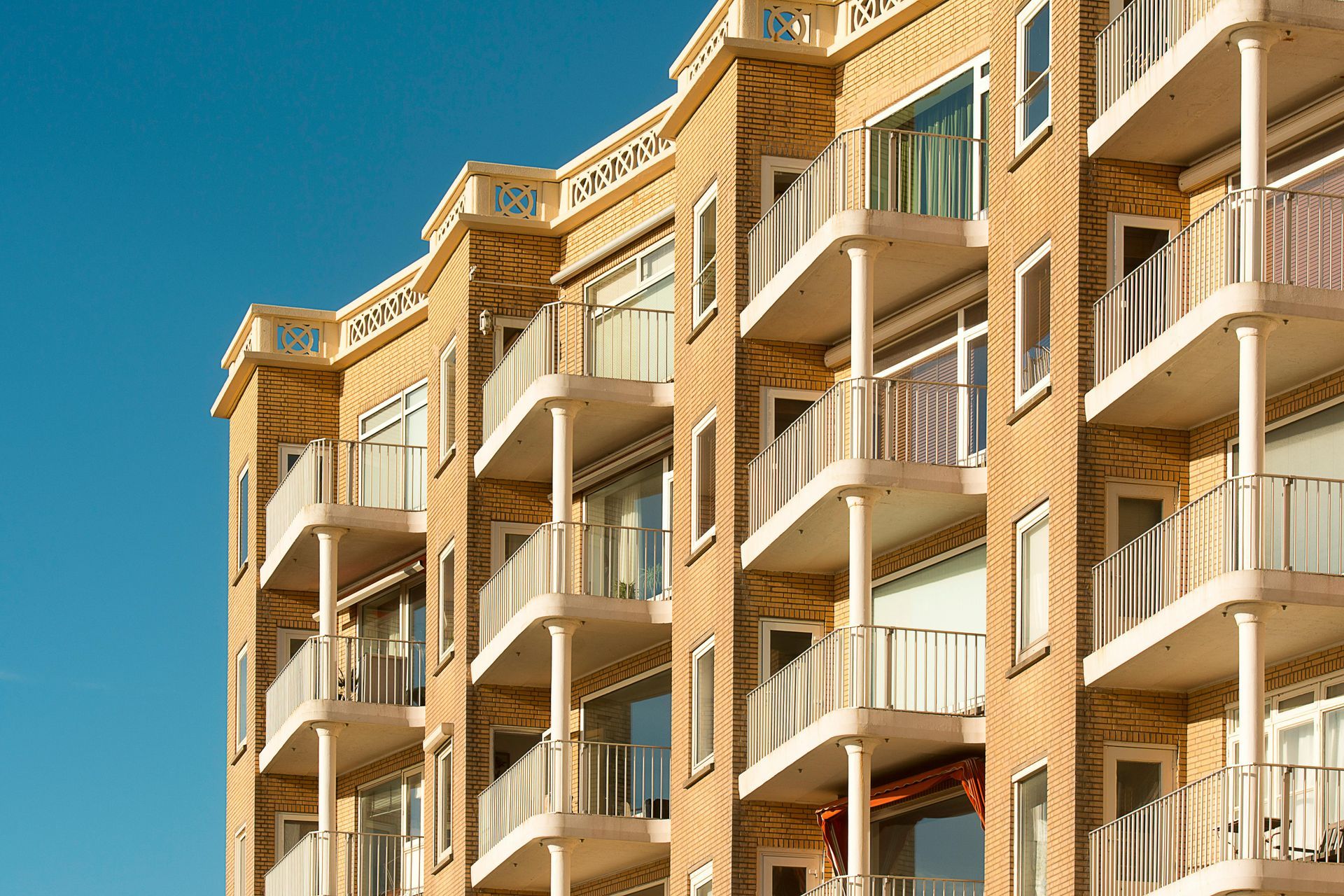 Tan apartment building with white balconies against a clear blue sky