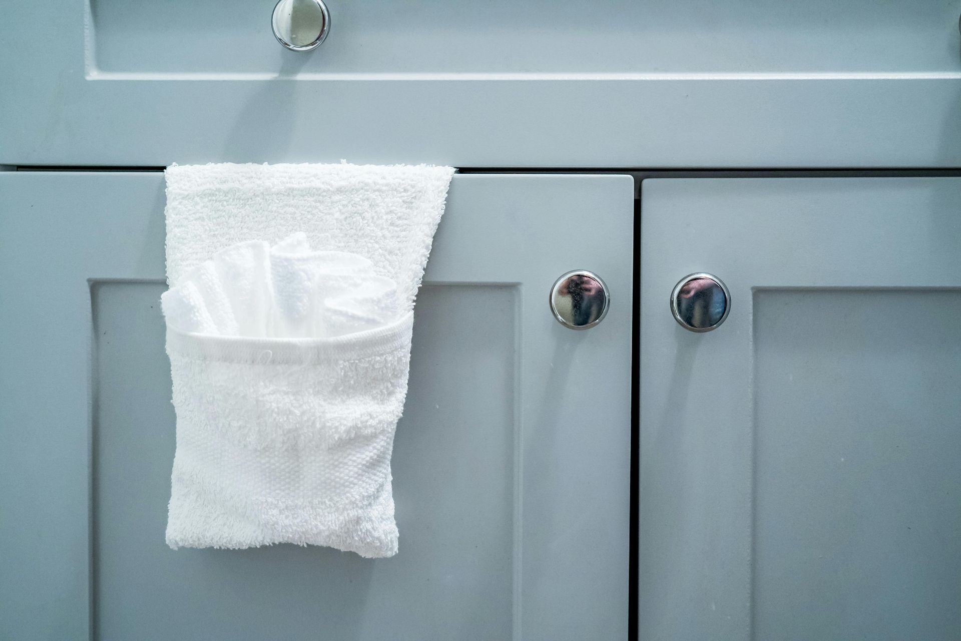 White cloth hanging on a chrome cabinet knob above gray cabinet doors