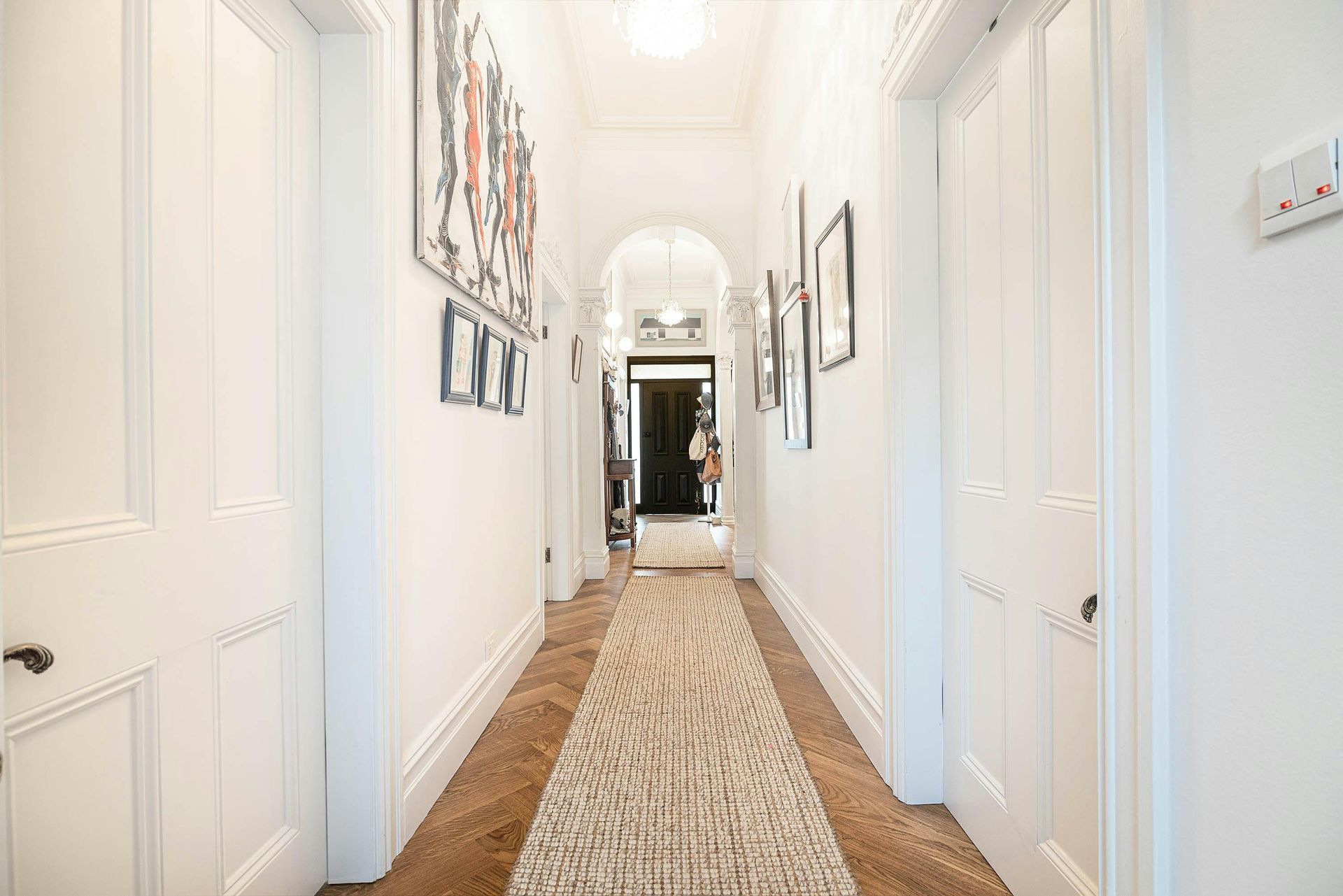 Bright hallway with white walls, framed art, and a long patterned runner rug in a home.