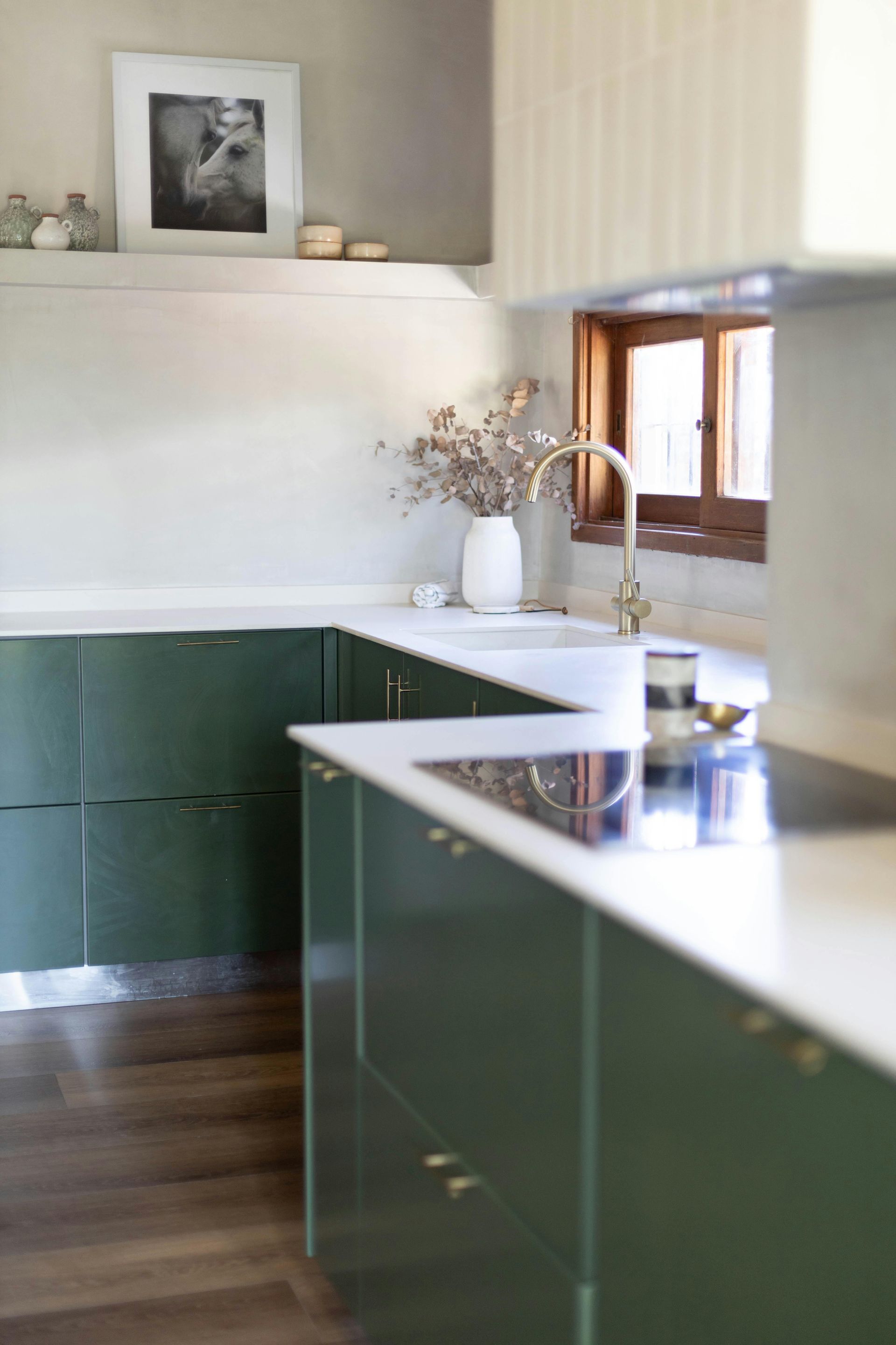 Modern kitchen with dark green cabinets, white countertops, and a window above the sink