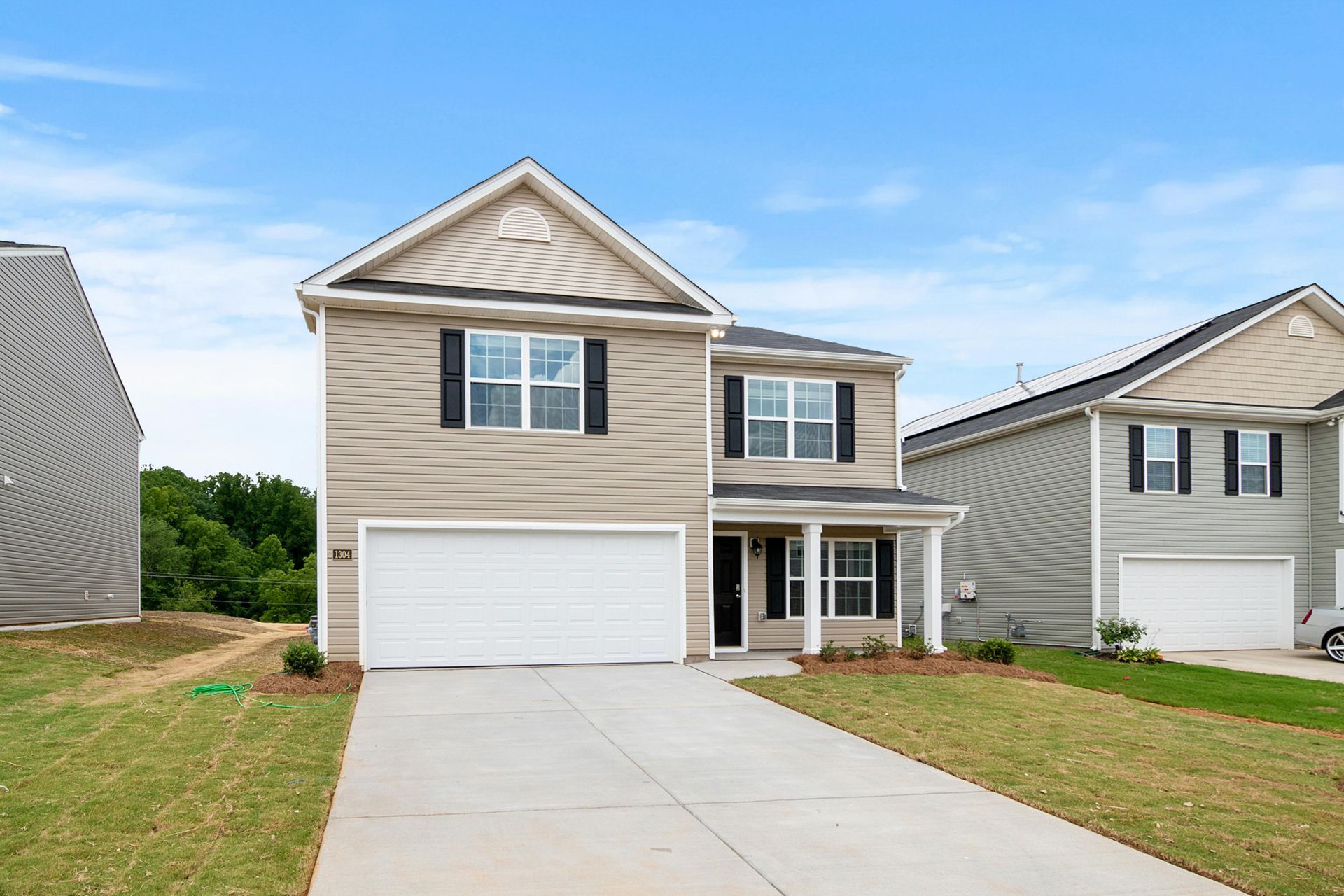 Suburban two-story beige house with white garage and driveway under a blue sky