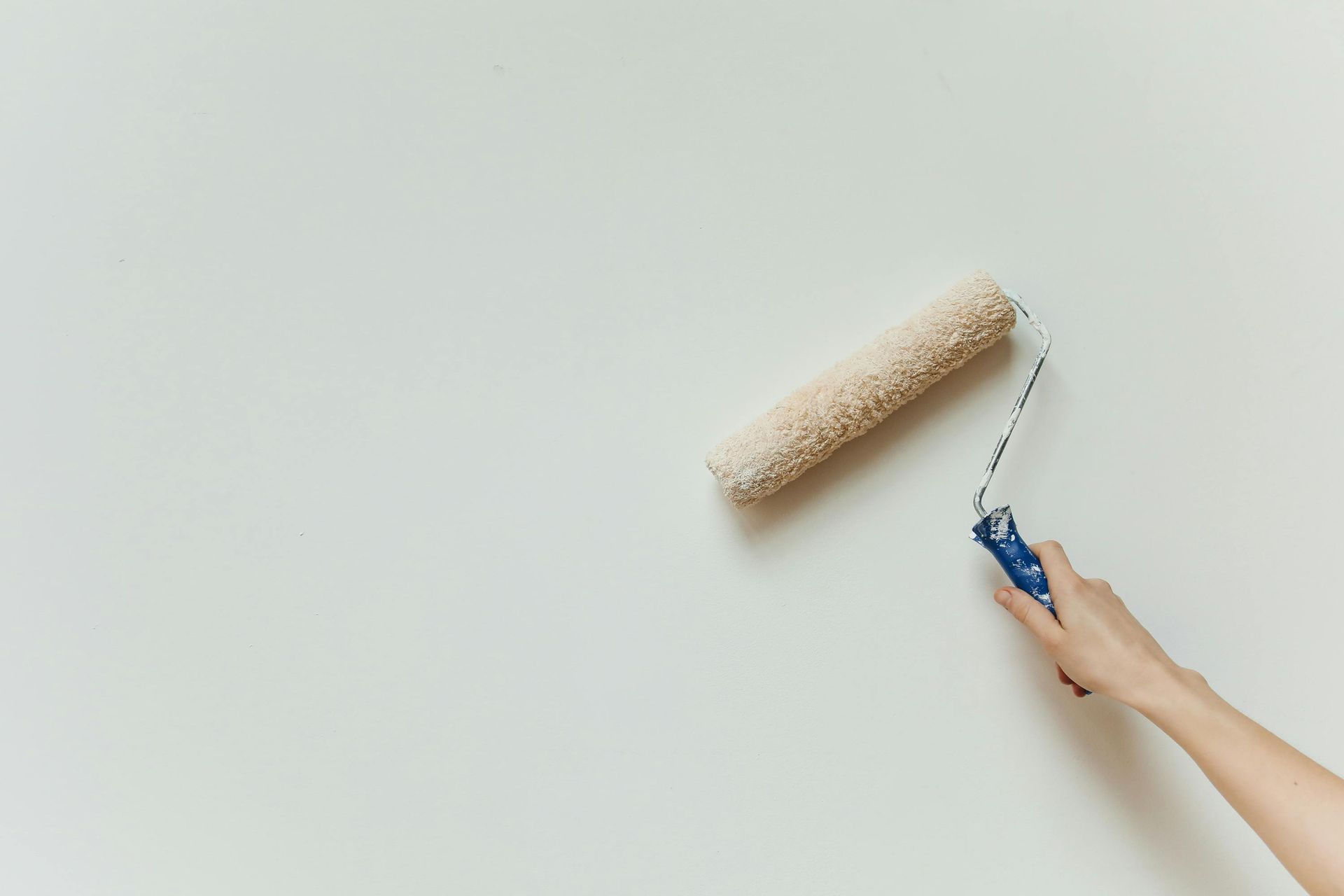 Hand holding a paint roller painting a white wall