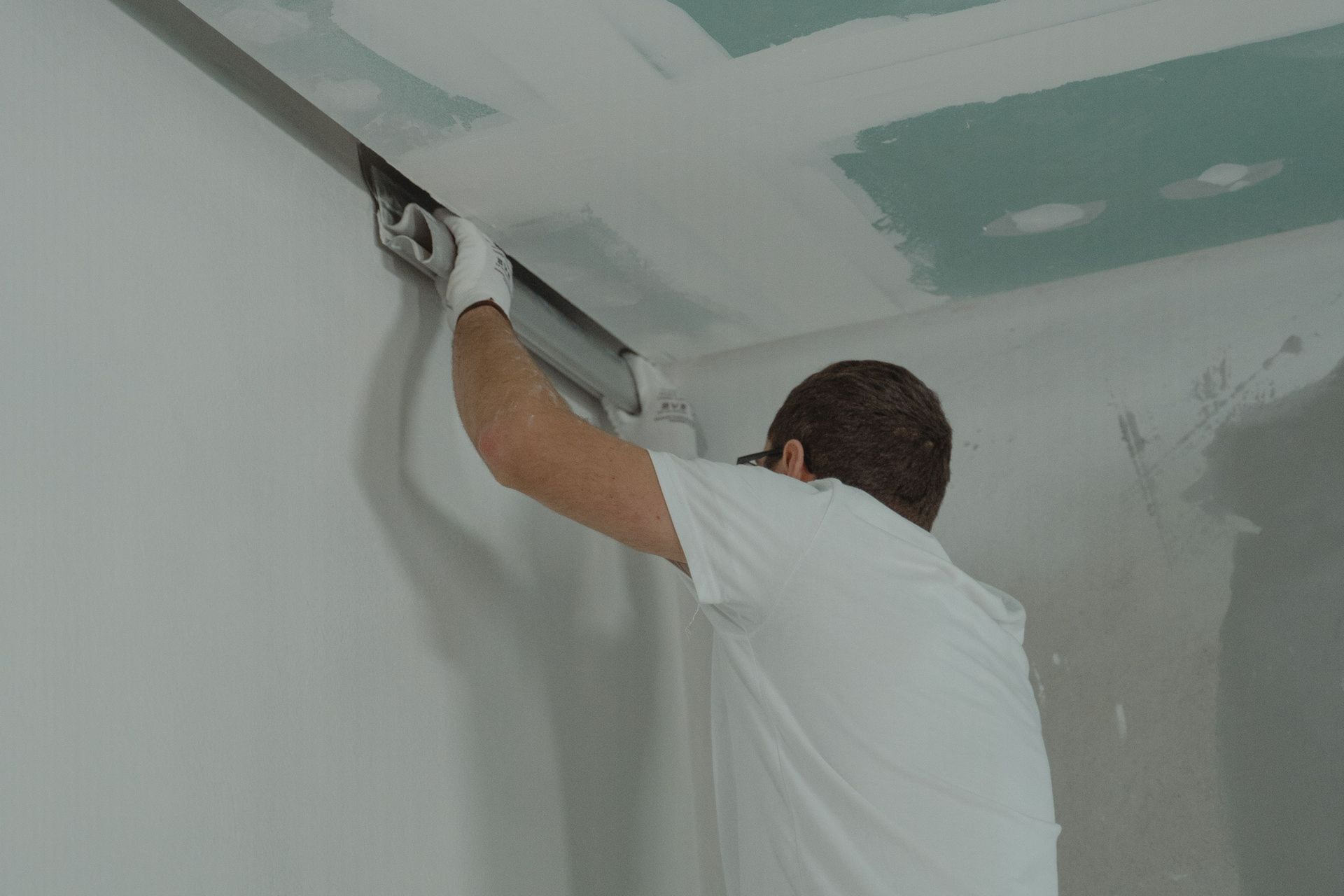 Person smoothing drywall compound on a ceiling with a trowel in an unfinished room