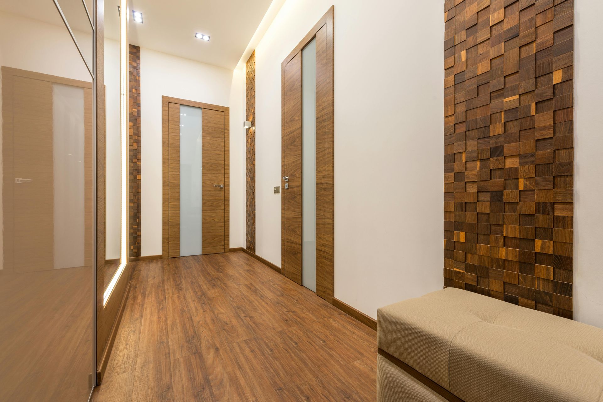 Modern hallway with wood floors, white walls, mirrored doors, and a decorative wood accent wall with a bench.
