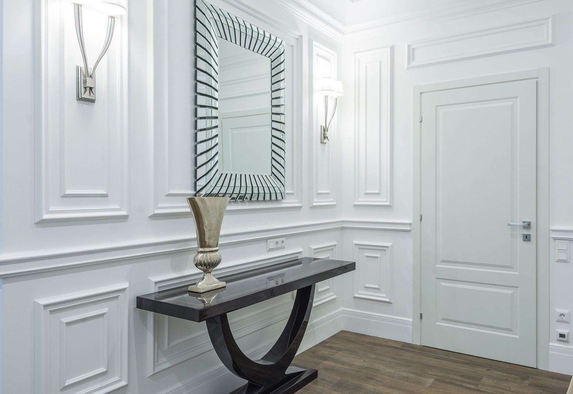 Elegant white entry hall with paneled walls, a console table, mirror, and wall sconce