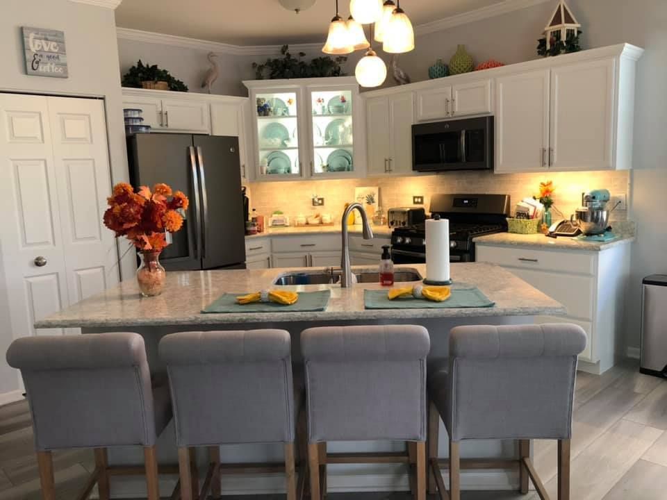 Bright modern kitchen with gray island, white cabinets, hanging lights, and vase of orange flowers
