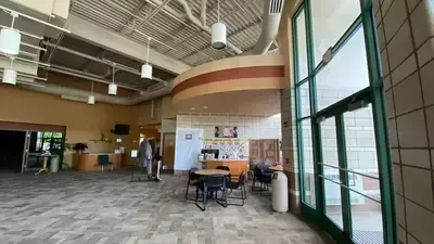 Spacious lobby with tables, chairs, tiled floor, high ceiling, and large windows on the right.
