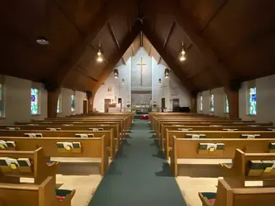 Empty church sanctuary with wooden pews, stained glass windows, and a cross at the altar.