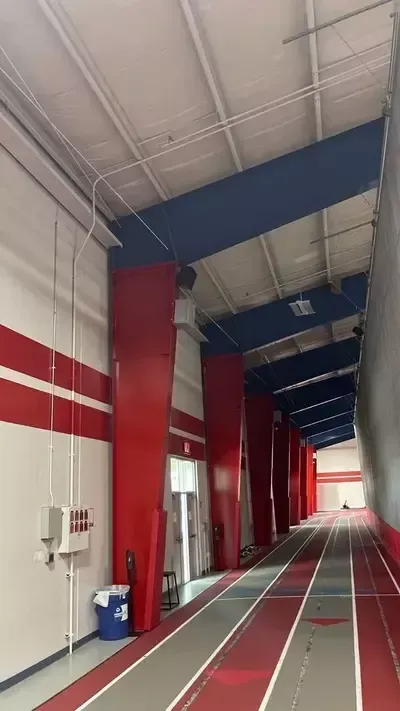 Long indoor sports hall with red-and-white walls, blue ceiling beams, and lane markings on the floor