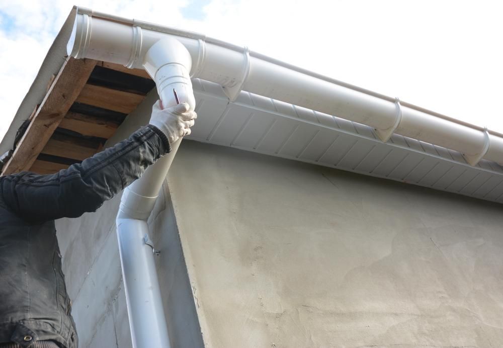 A Man Is Installing A White Gutter On The Side Of A House — Gold Coast City Plumbing In Helensvale, QLD