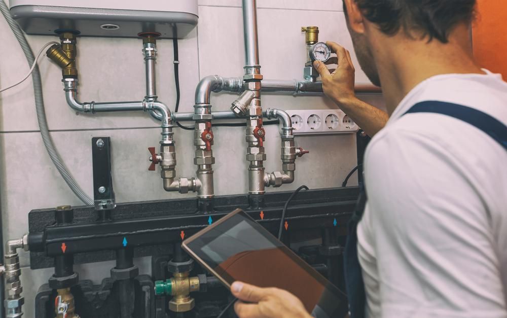 A Man Is Working On A Pipe System While Holding A Tablet — Gold Coast City Plumbing In Runaway Bay, QLD