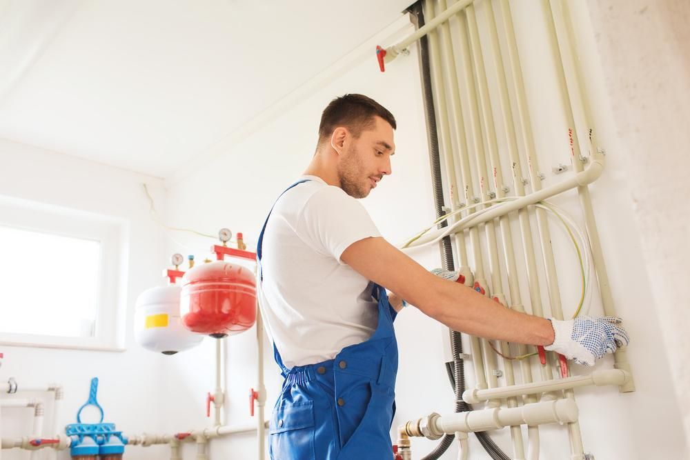 A Man Is Working On A Heating System In A Room — Gold Coast City Plumbing In Helensvale, QLD