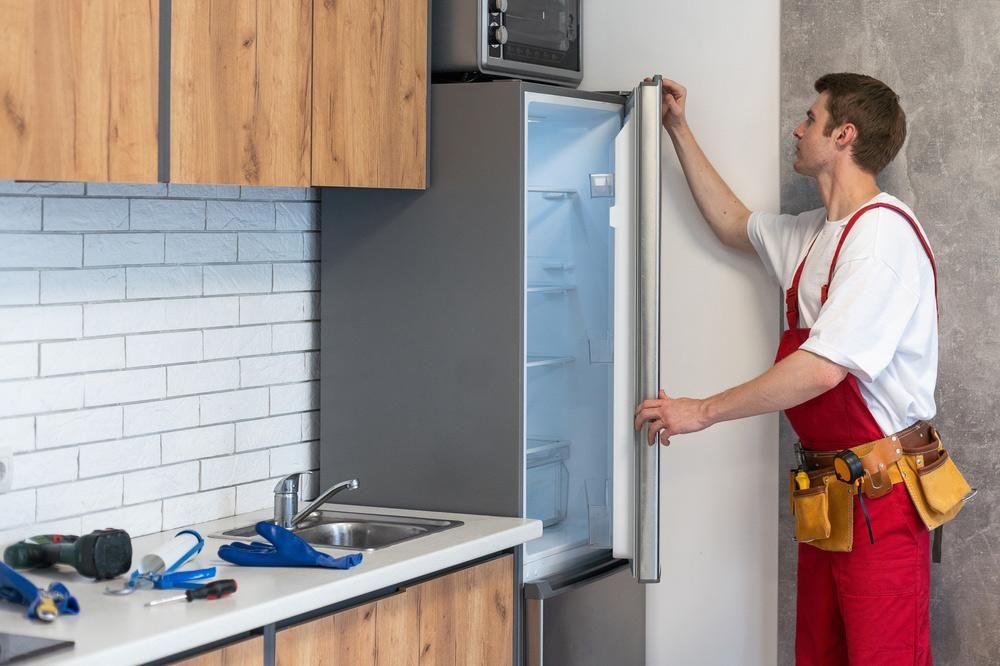 A Man Is Fixing A Refrigerator In A Kitchen — Gold Coast City Plumbing In Helensvale, QLD
