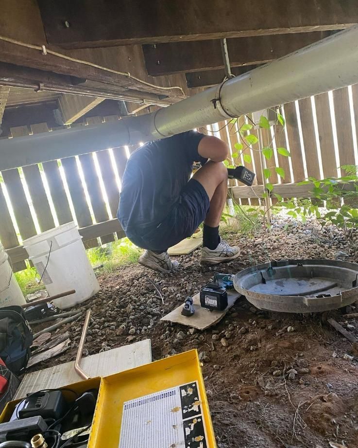 A Man Is Kneeling Under A Pipe In A Basement — Gold Coast City Plumbing In Helensvale, QLD