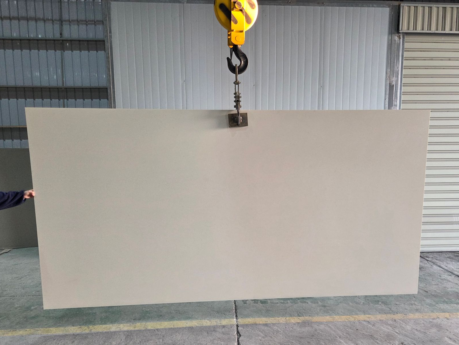A Large, Solid Light Beige Stone Slab is Suspended by a Yellow Industrial Crane Hook — Better Stone in Caloundra West, QLD