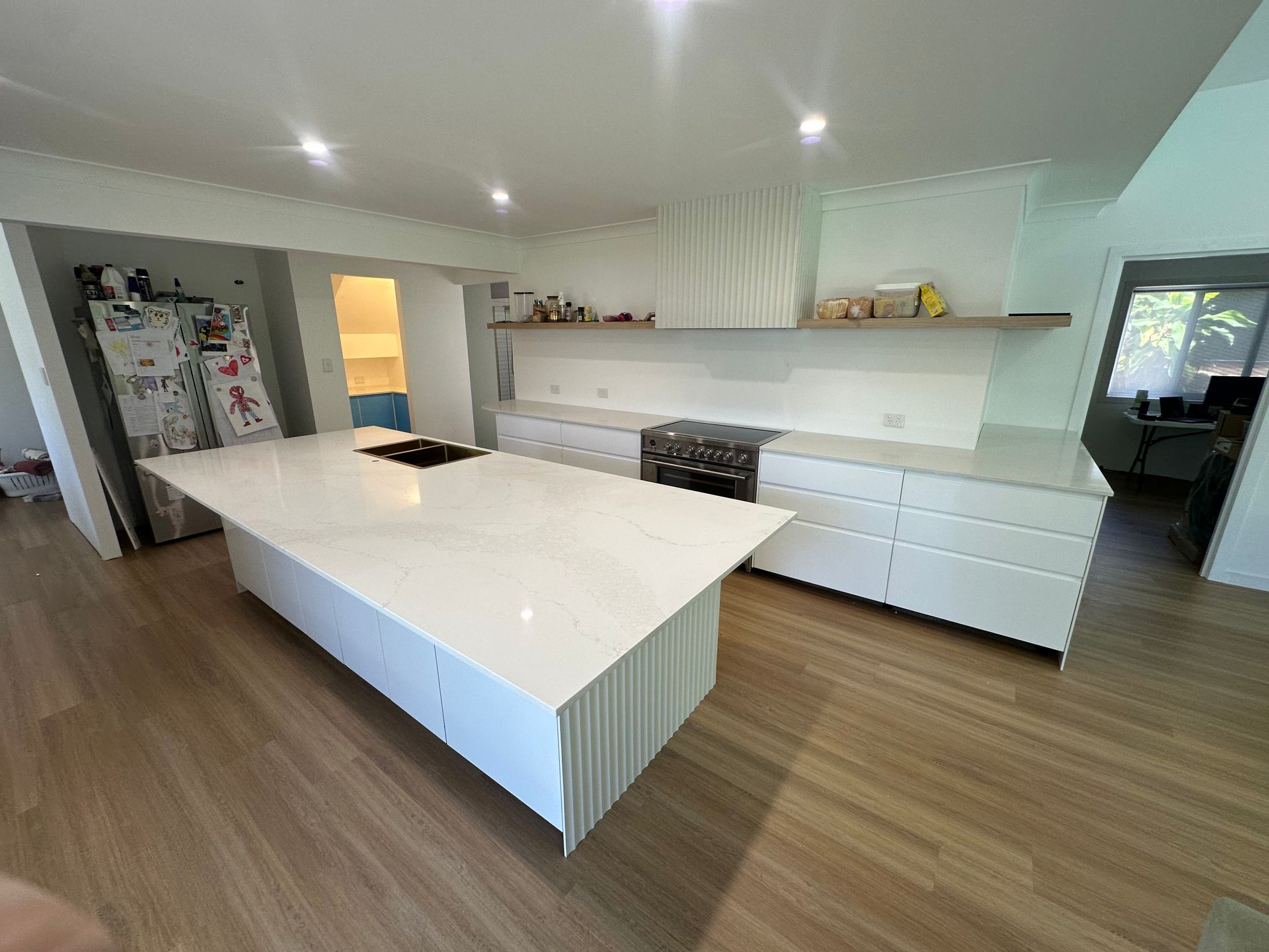 Modern kitchen with white cabinets, island, cooktop, and wooden floors.