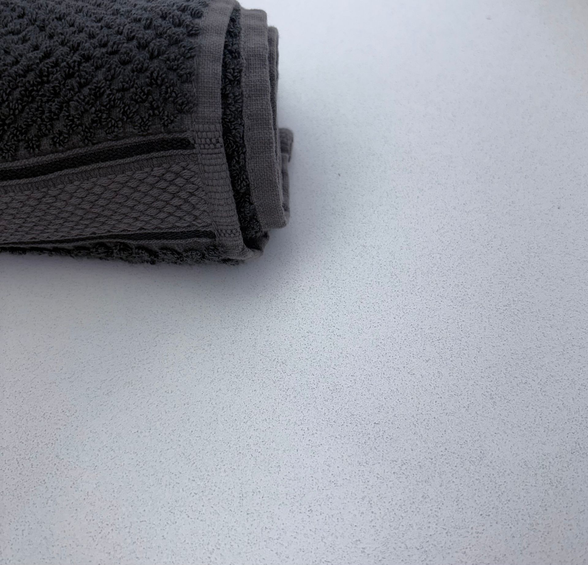 Rolled dark gray towel on a white speckled surface.