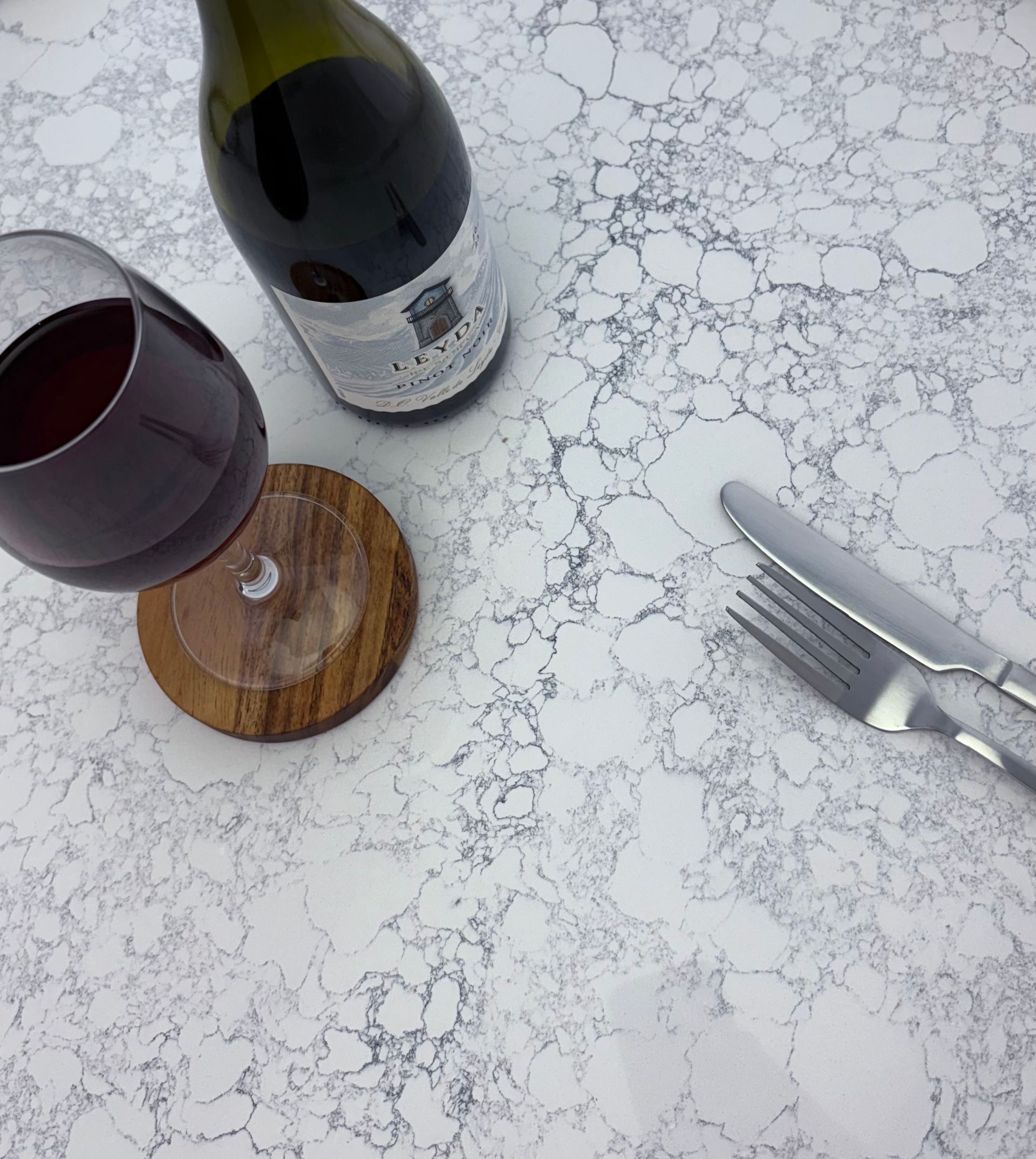 Wine glass and bottle on a marble-patterned surface with silverware and a coaster.