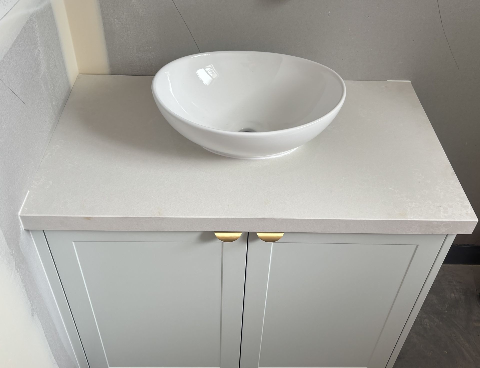 White vessel sink on a light gray cabinet with gold handles.