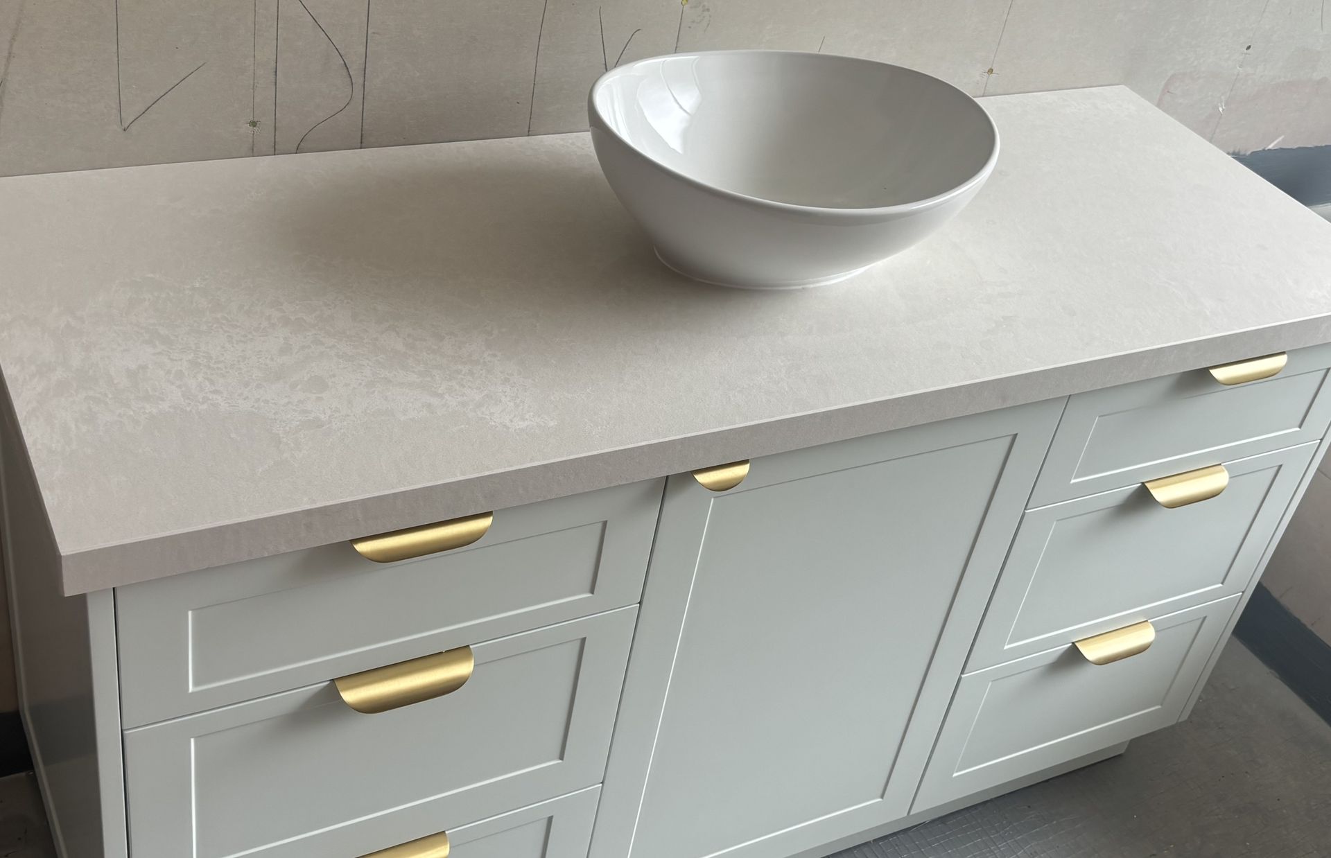 Vanity with white countertop, vessel sink, and gray cabinets with gold hardware.