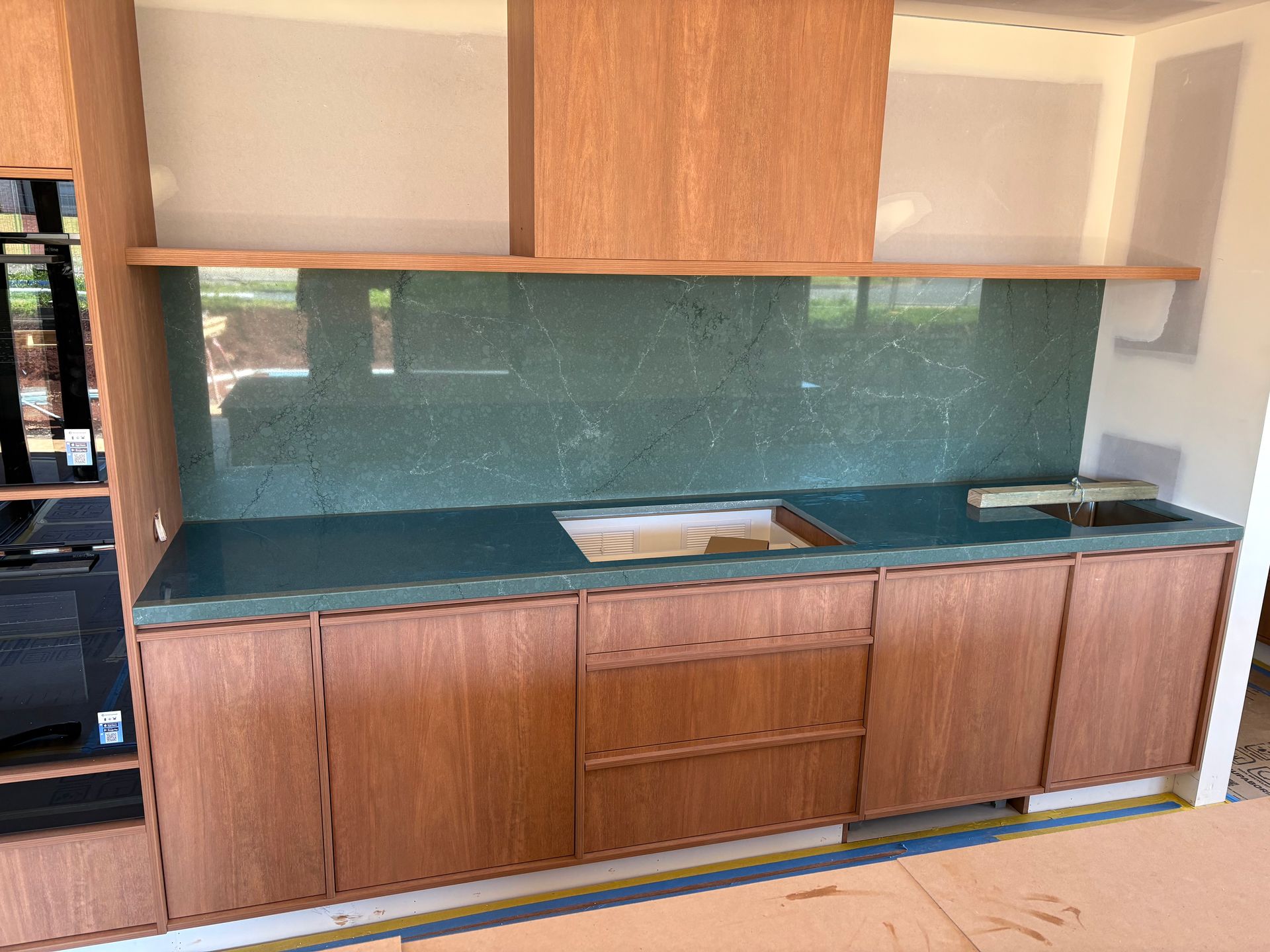 Kitchen cabinets with a green backsplash and countertop. Wooden cabinets. A stainless steel sink is visible.