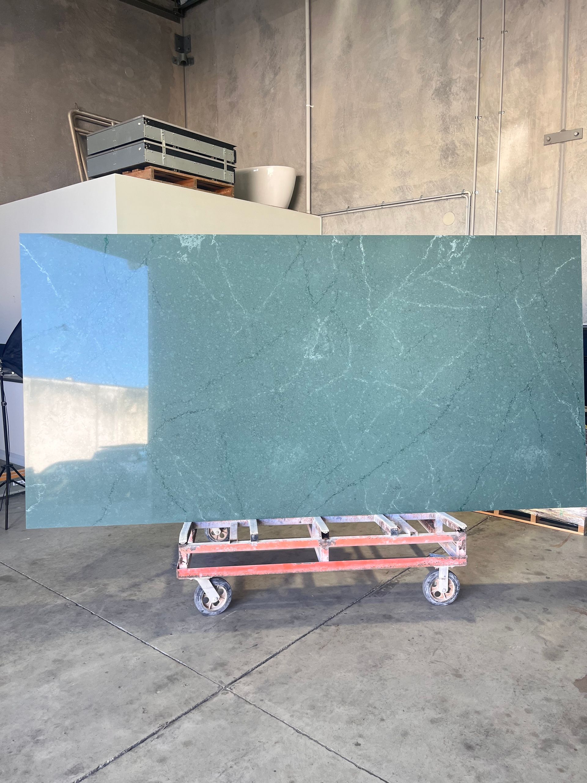 Large green countertop slab on a red wheeled cart in a warehouse.