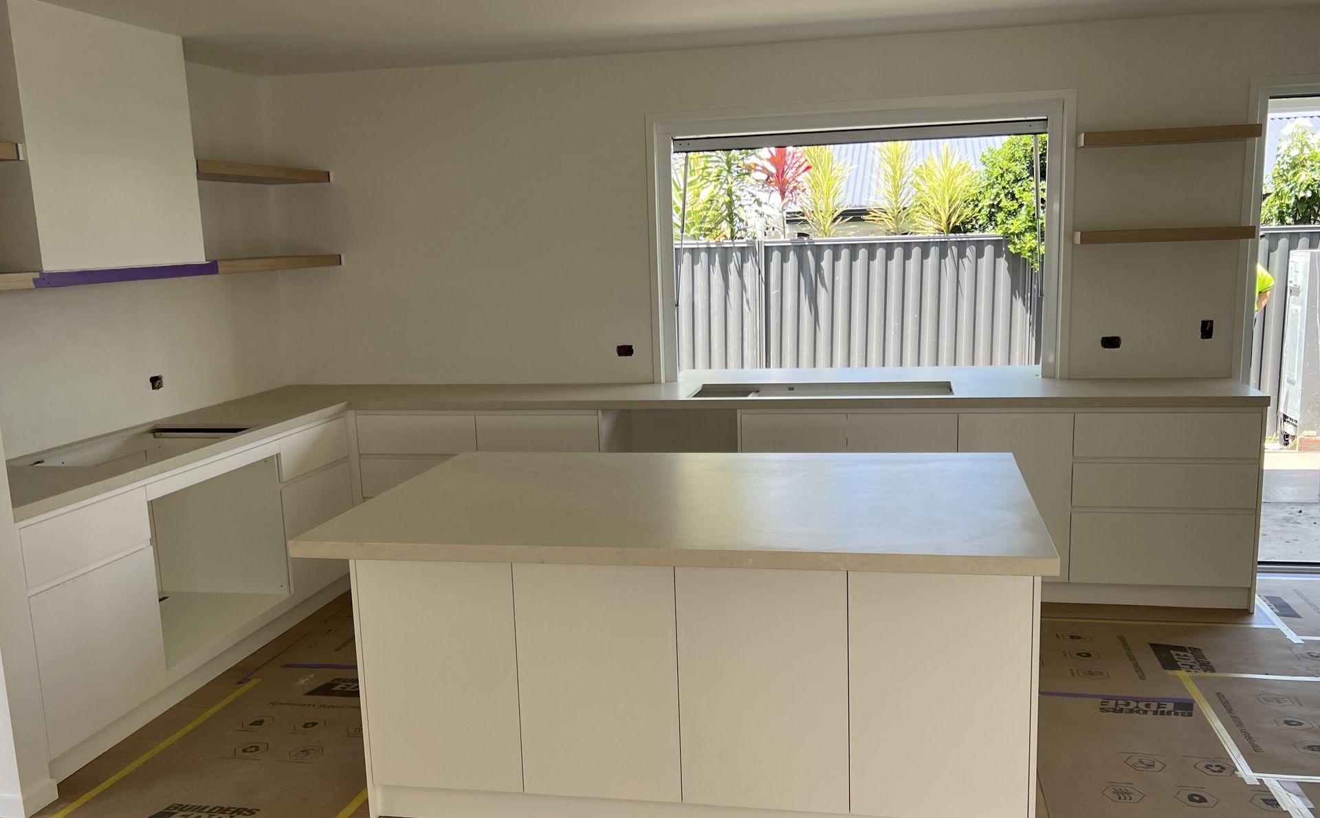 White kitchen with island, countertops, cabinets, and a window overlooking a fence.