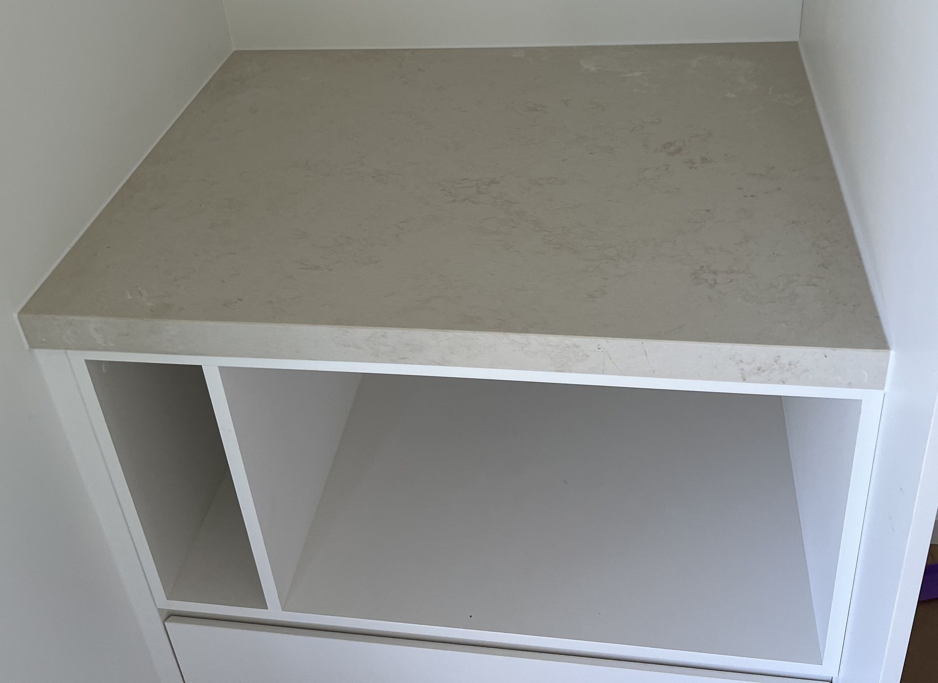 White cabinet with beige countertop and open shelves, set against white walls.