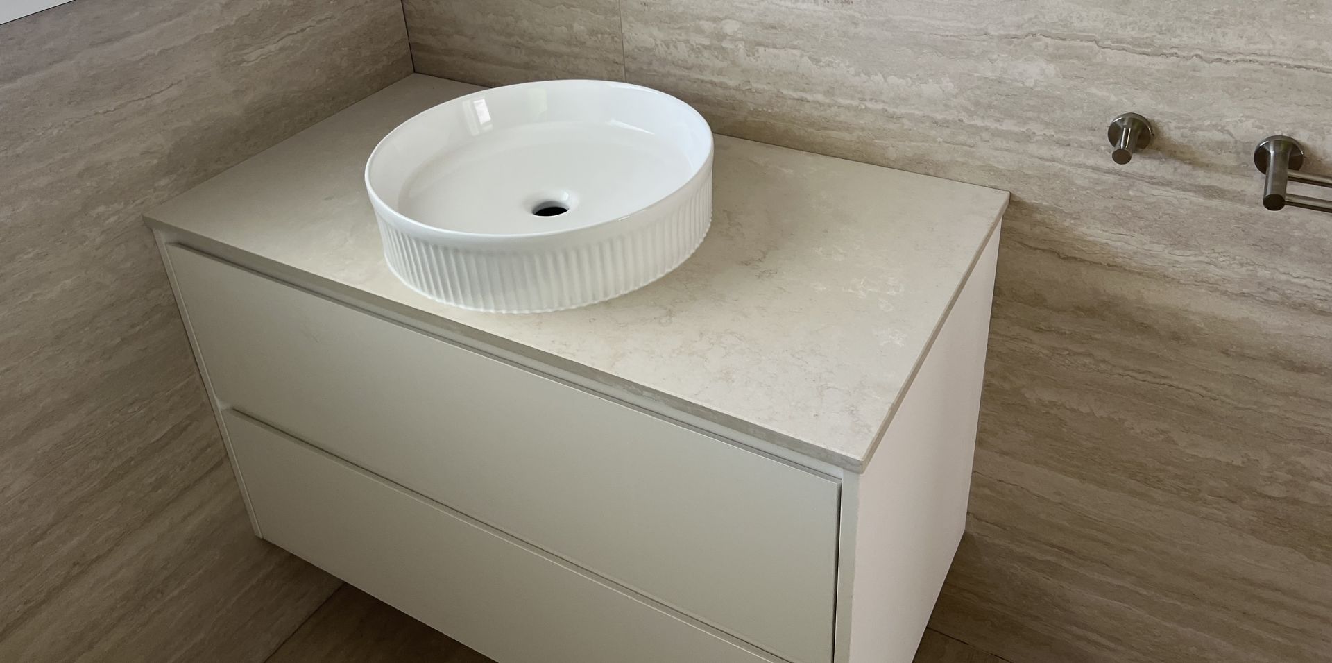 Bathroom vanity with a round white sink on a light-colored countertop. The vanity has two drawers.