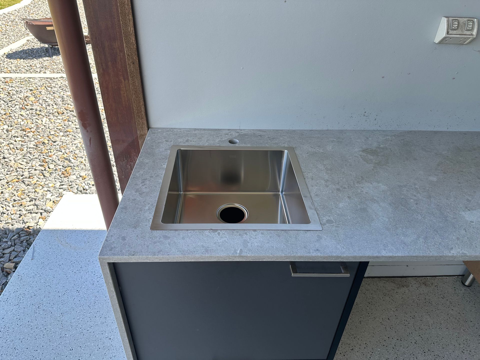 Outdoor concrete countertop with stainless steel sink, black cabinet, and white wall.
