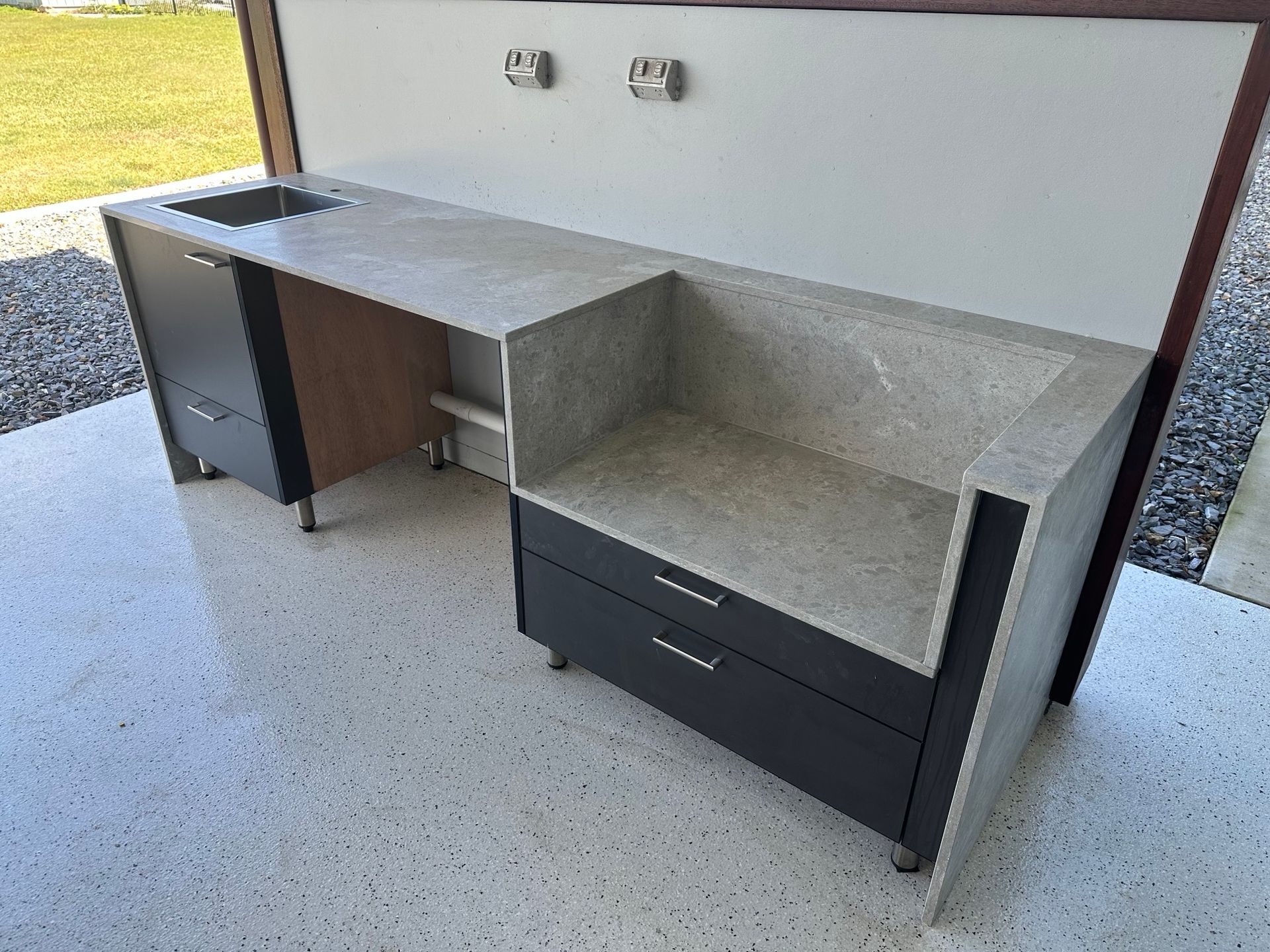 Outdoor concrete countertop with built-in sink and cabinets. Grey and black cabinets. Wall mounted above.