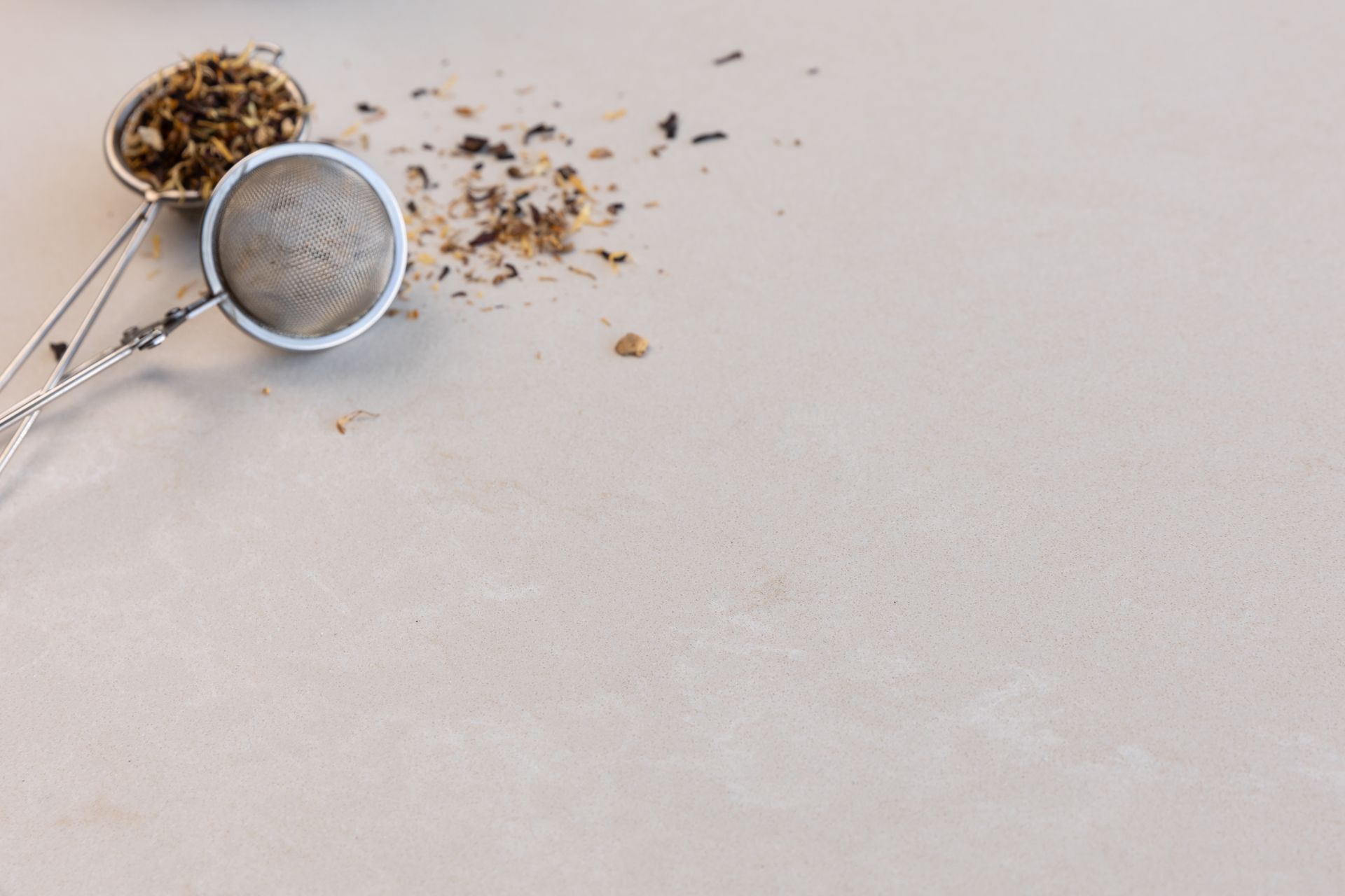 Tea strainer with loose tea leaves on a light-colored surface.