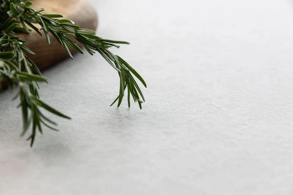 A Sprig of Rosemary is Sitting on a White Surface Next to a Wooden Cutting Board — Better Stone in Caloundra West, QLD