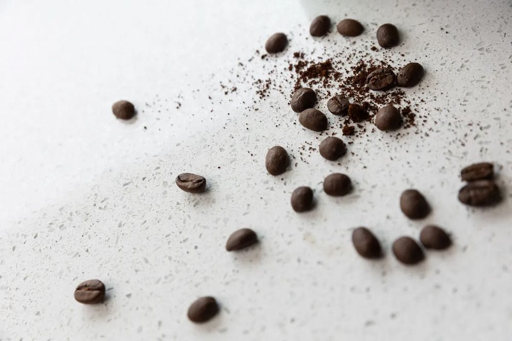 Coffee beans and ground coffee are scattered on a white surface. — Better Stone in Caloundra West, QLD