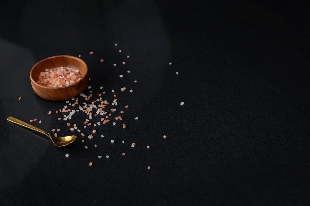 A Bowl of Pink Salt and a Gold Spoon on a Black Surface — Better Stone in Caloundra West, QLD