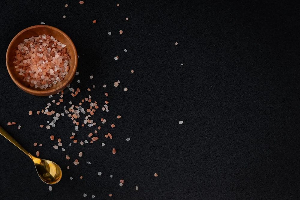 A Bowl of Pink Salt and a Gold Spoon on a Black Background — Better Stone in Caloundra West, QLD