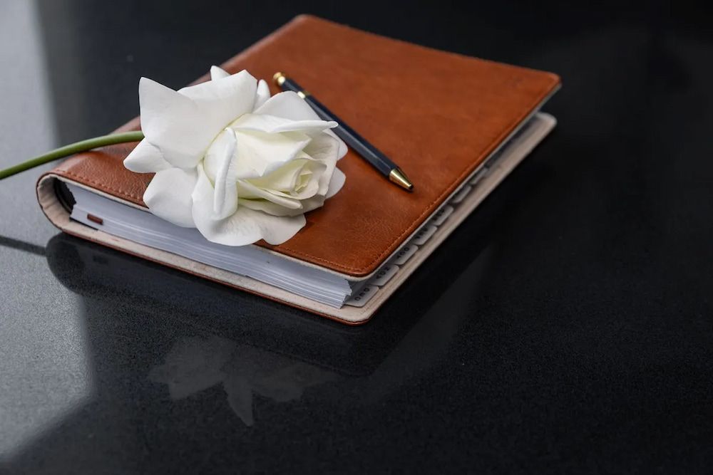 A White Rose is Sitting on Top of a Notebook With a Pen — Better Stone in Caloundra West, QLD